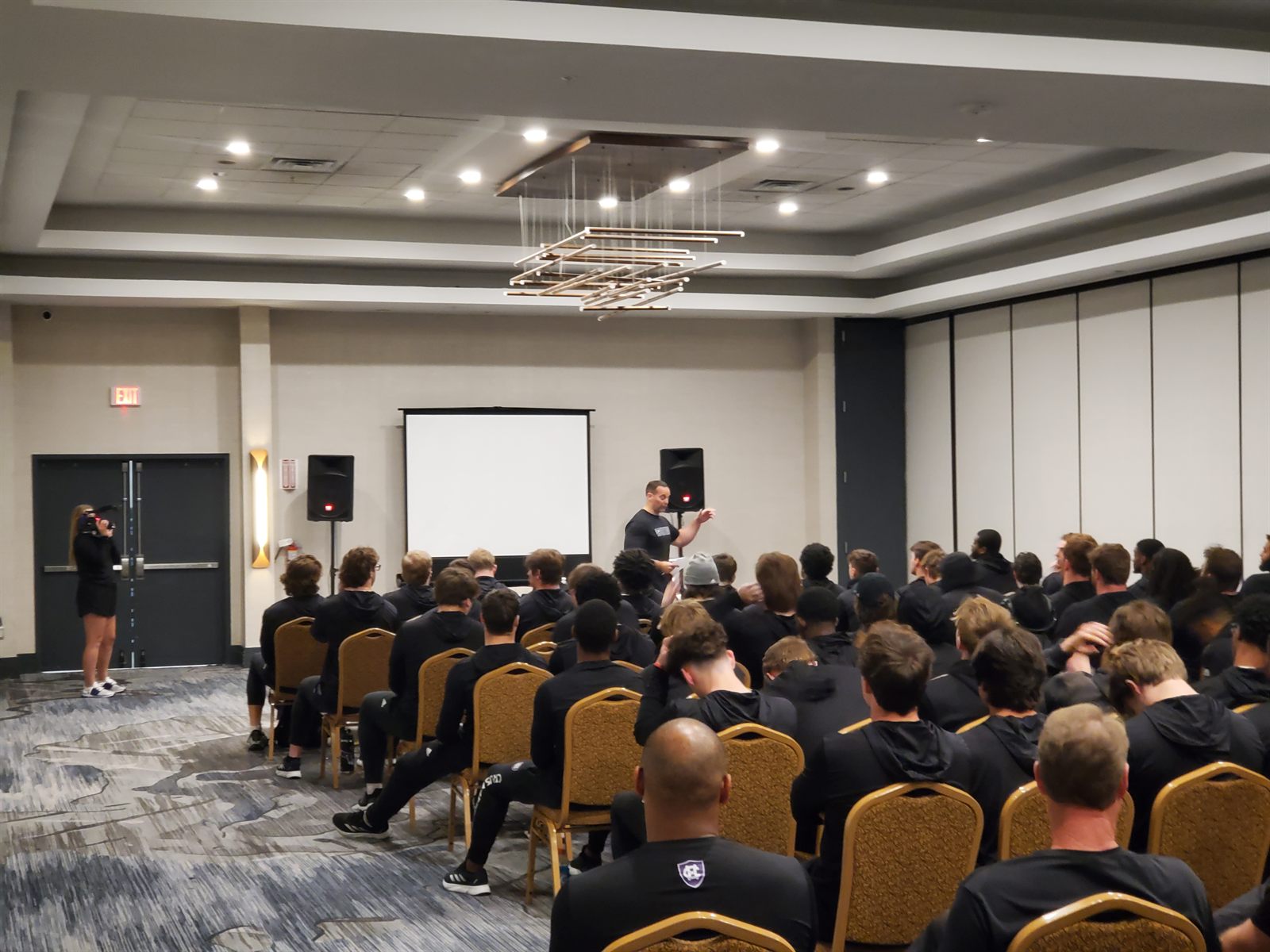 A Holy Cross team meeting — players seated facing the front of the room as a coach presents from a single screen.
